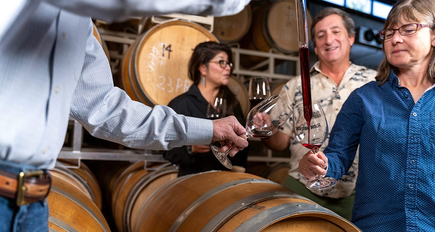 People tasting wine in winery with barrels.