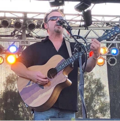 Musician playing guitar on stage with microphone.