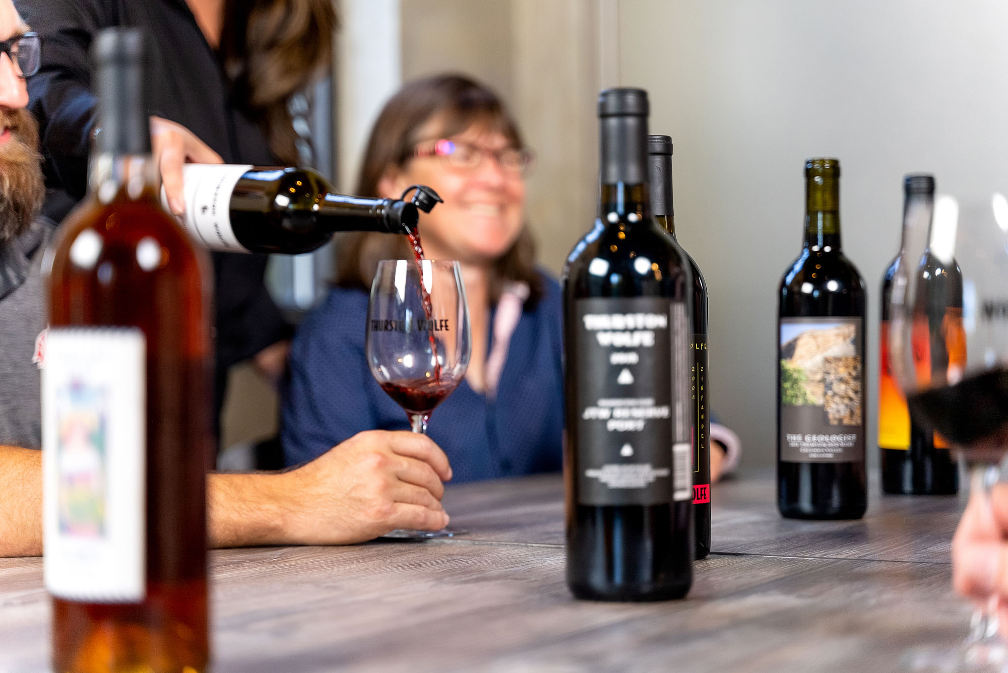 Wine pouring into glass on table with bottles.