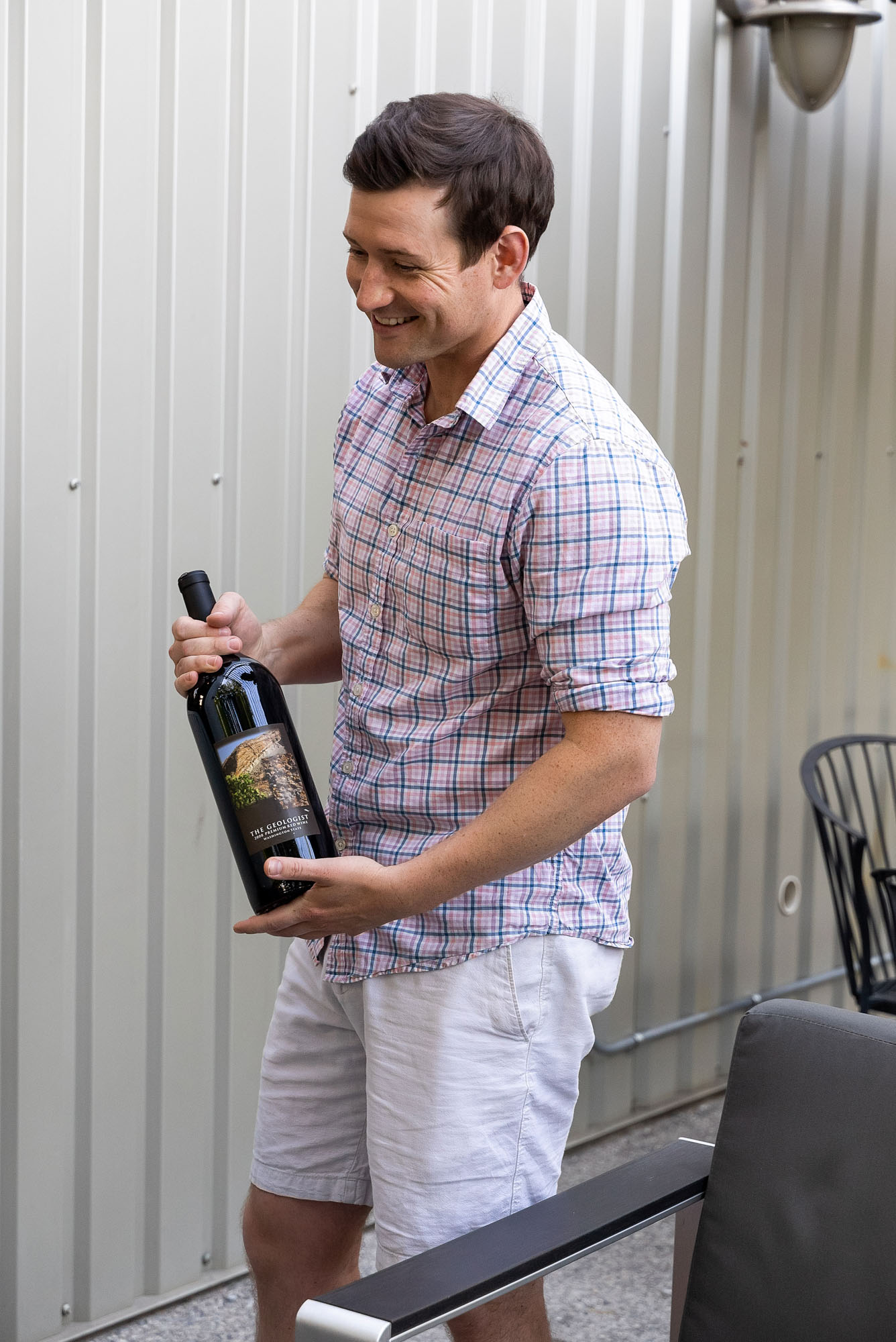 Smiling man holding wine bottle outdoors.