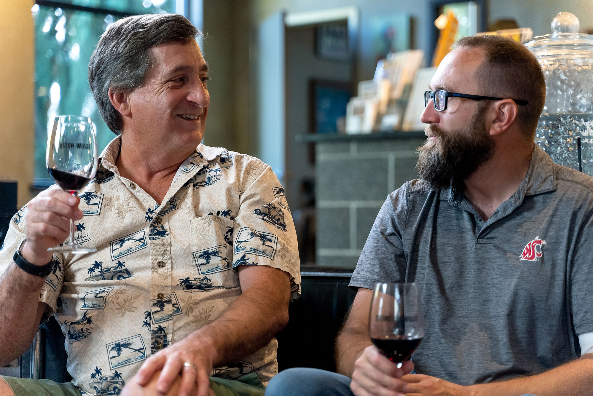 Two men chatting and drinking red wine indoors.