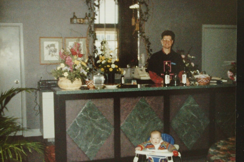 Man standing behind counter, baby in walker.