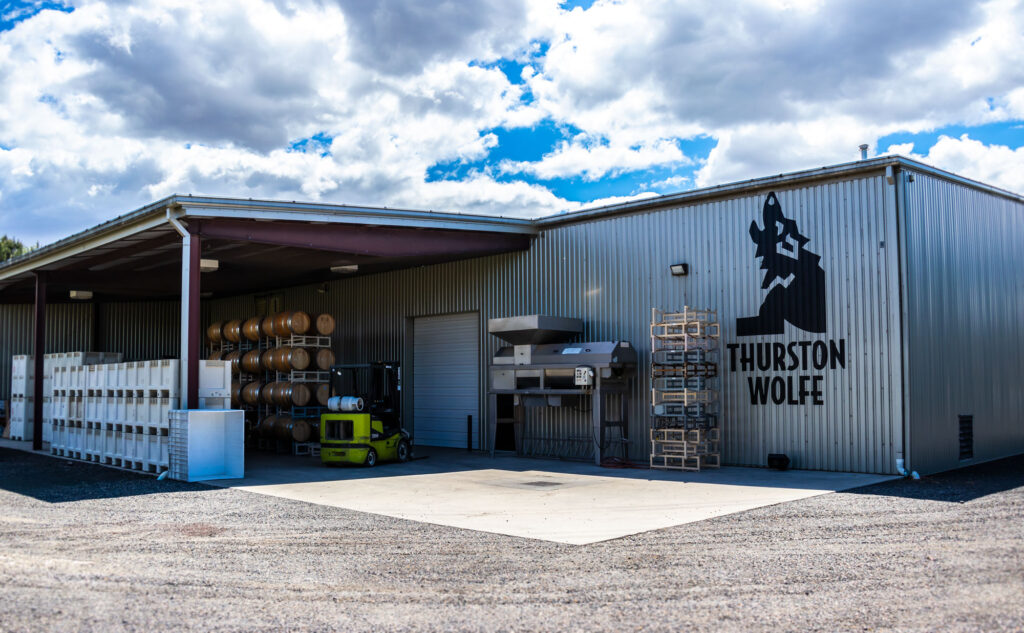 Winery building with barrels and equipment outside.
