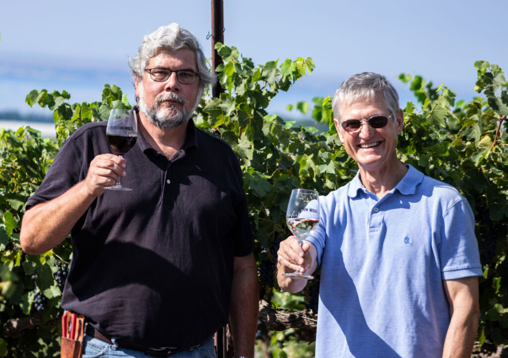 Two men toasting in vineyard with wine glasses.