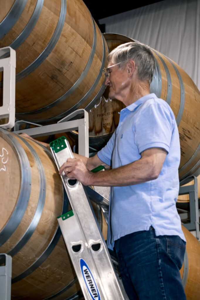 Man inspects wine barrels on ladder