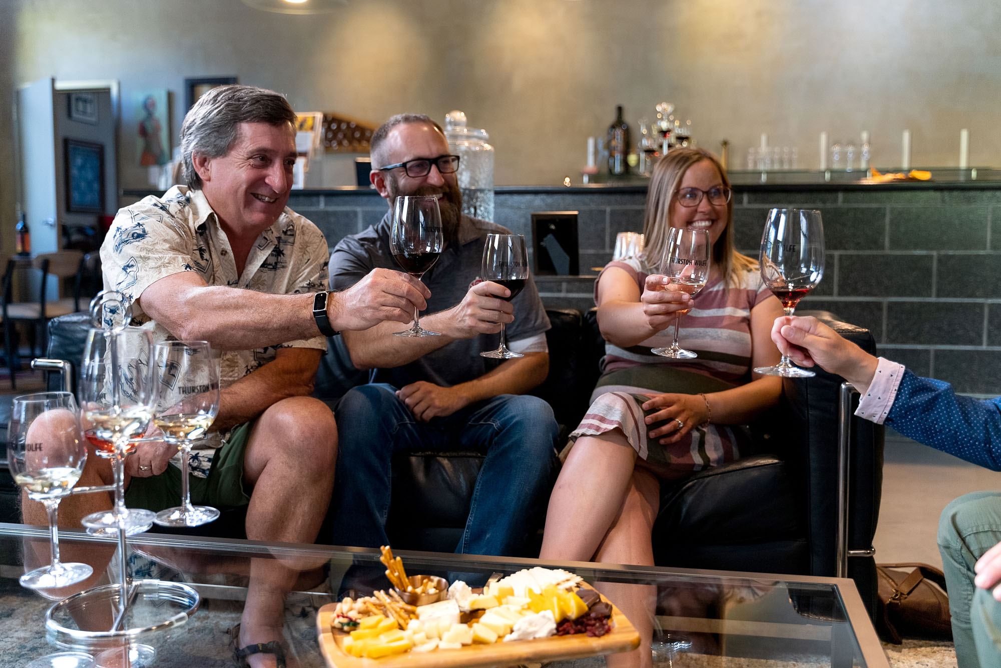 People toasting wine glasses with cheese platter.