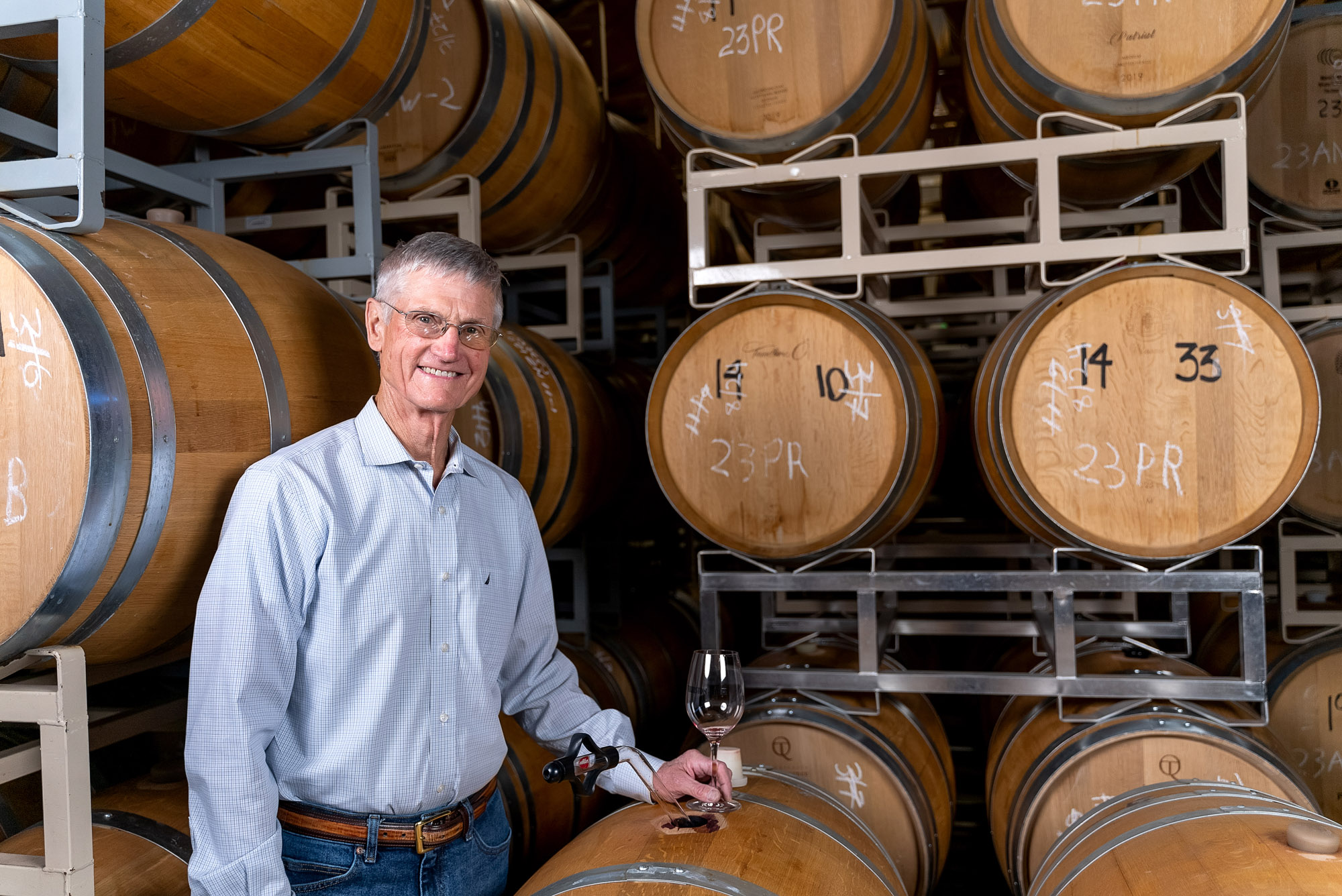 Man in wine cellar with oak barrels and glass.